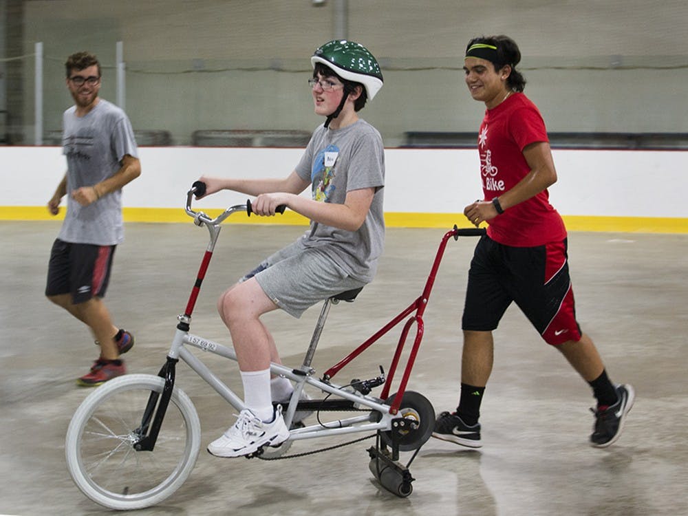 Quentin West, left, and Solustrisimo Jr. Garcia, assist Beau Jent, 12, riding the bike during the iCan Bike camp event held at Frank Southern Ice Arena on Monday evening. West said this is another good way to help this population that just want to be like everyone else. 