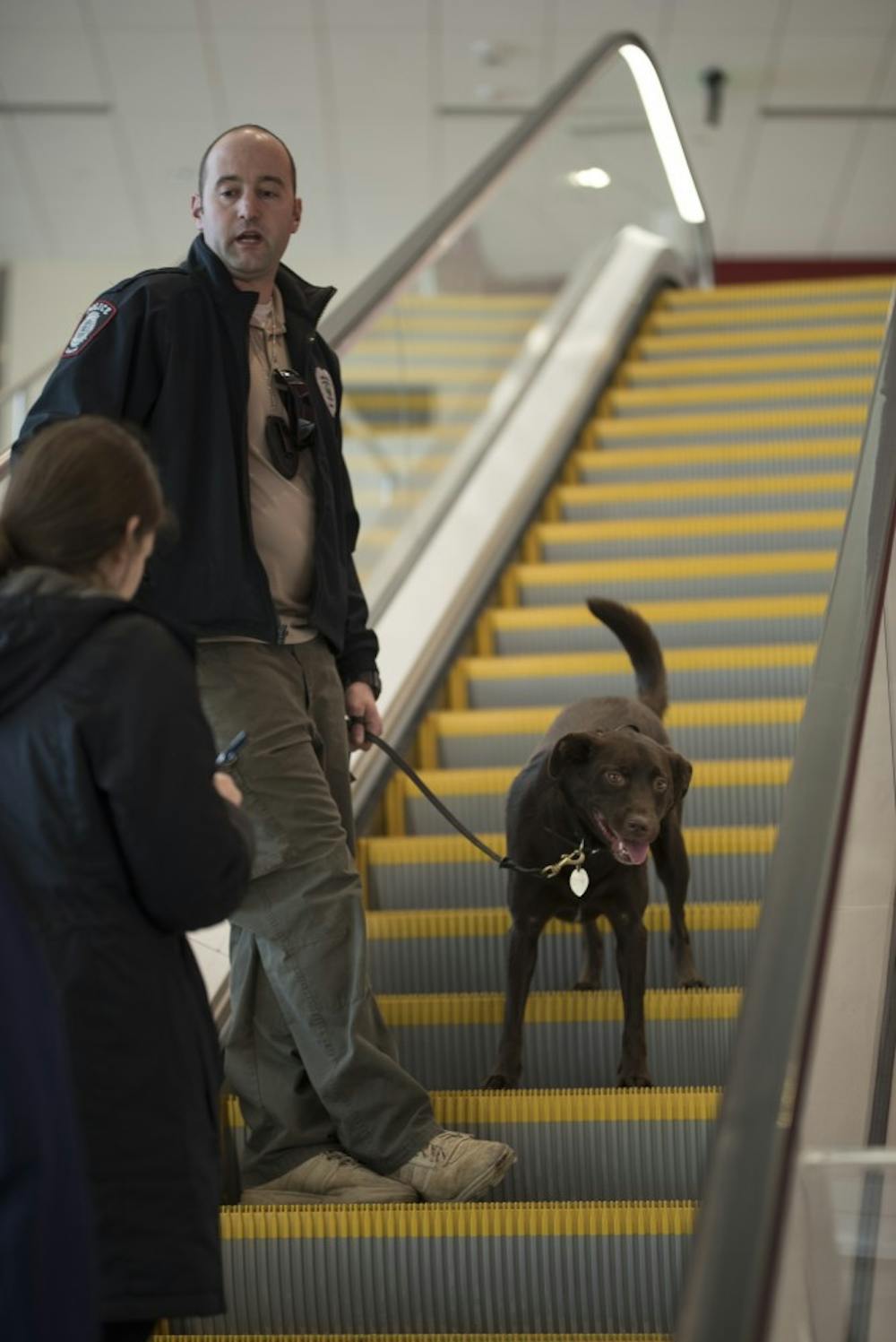 IUPD officer Ryan Skaggs and his dog Zeus ride up the escalator in Simon Skjodt Assembly Hall as Zeus checks for bombs before the basketball game Tuesday. Zeus was a rescue dog and is the department's only trained bomb search dog in Bloomington.&nbsp;