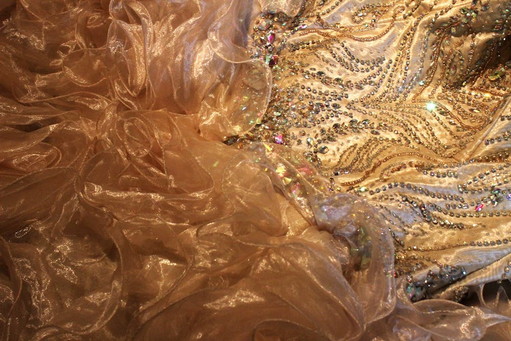 Backstage，Quinceañera礼服于9月26日休息。26岁时，在Kirkwood Avenue的第15届年度Fiesta deOtoño跑道准备跑道。这件衣服是米色，装饰着多彩宝石。