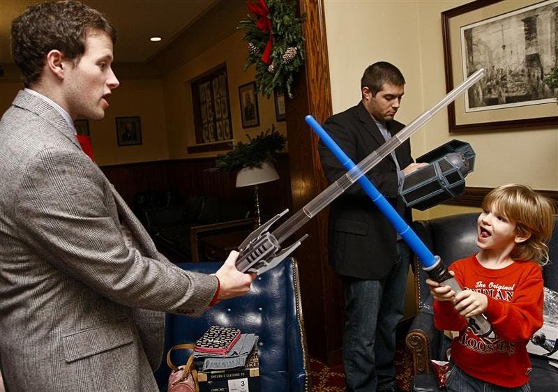 Junior Bryan Mansfield, left, and Elijah Christenberry duel with light sabers, while junior Kidd Cardillo, background, puts together a Tie-Fighter on Tuesday evening at the Alpha Tau Omega Second Annual Holiday Dinner. The brothers invited children from the Boys and Girls Club to have dinner and bought the children presents.