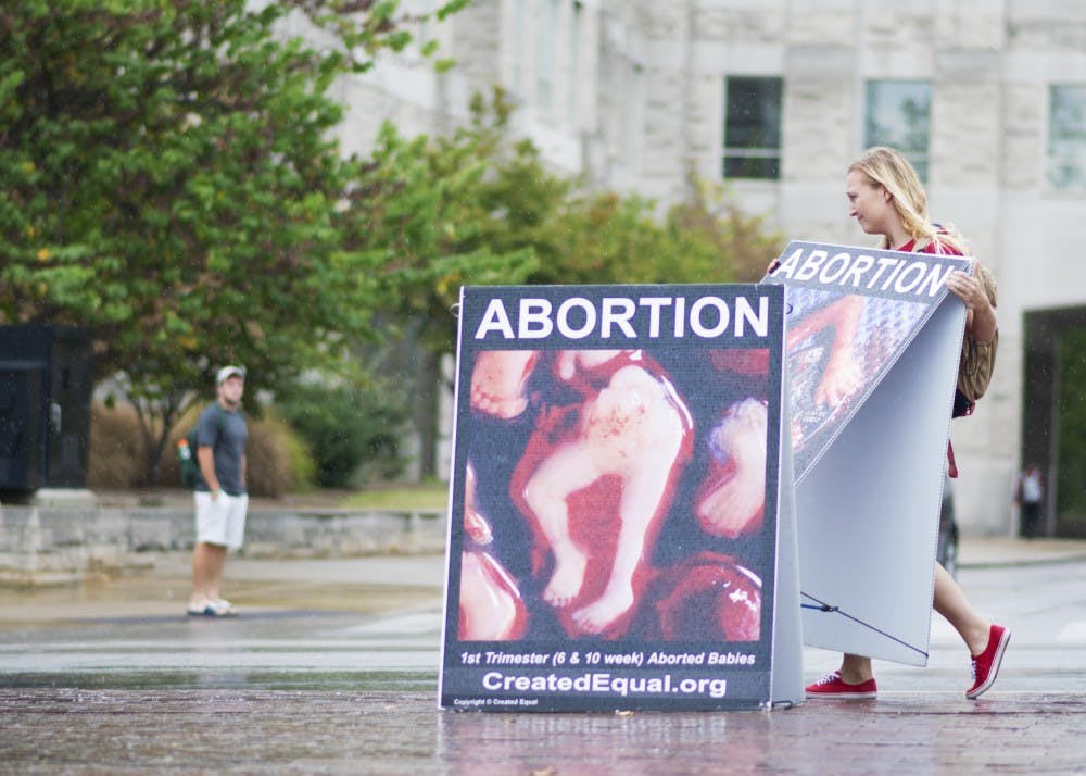 Junior Jenna Fisher, president of Students for Life at IU, moves a sign out of the rain Wednesday afternoon at the intersection of 10th Street and Fee Lane. Students for Life at IU partnered with Created Equal to place signs at the intersection protesting abortion.