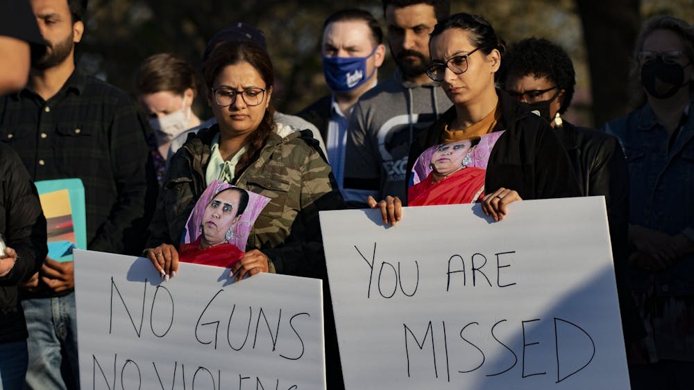 Attendees of a vigil in honor of those killed at the FedEx Ground shooting hold signs April 16, 2021, at Krannert Park in Indianapolis. Family members of the victims filed a lawsuit against FedEx for negligence.