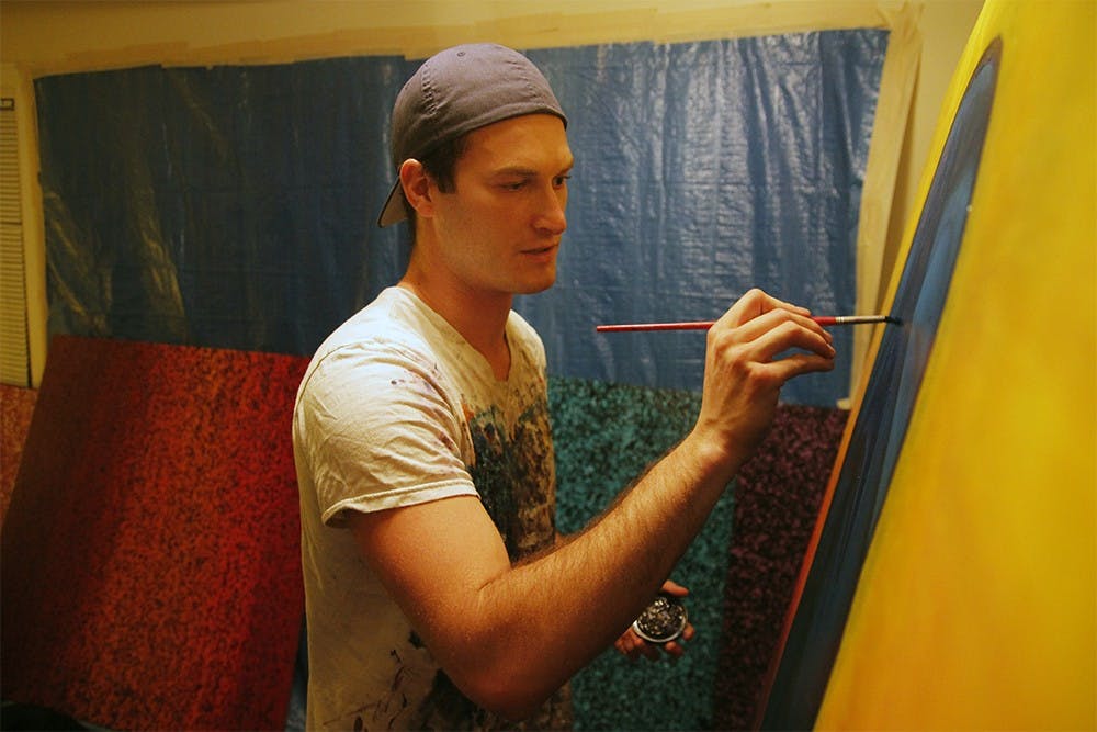 Adam Shapiro smiles as he works on one of his paintings on Monday evening in his studio. Shapiro descibes his art as "abstract expressionism" and says he has no other influences for his work other than life.