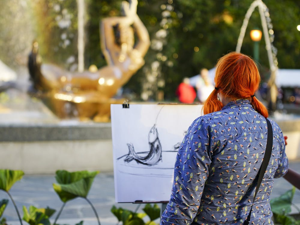 WFIU employee Kayte Young composes her sketch of Showalter Fountain as the sun sets during the First Thursdays festival Sept. 7, 2017, in the Fine Arts Plaza. ﻿First Thursdays&#x27; artist row is a way for students and community members to show their work and sell it to attendees.