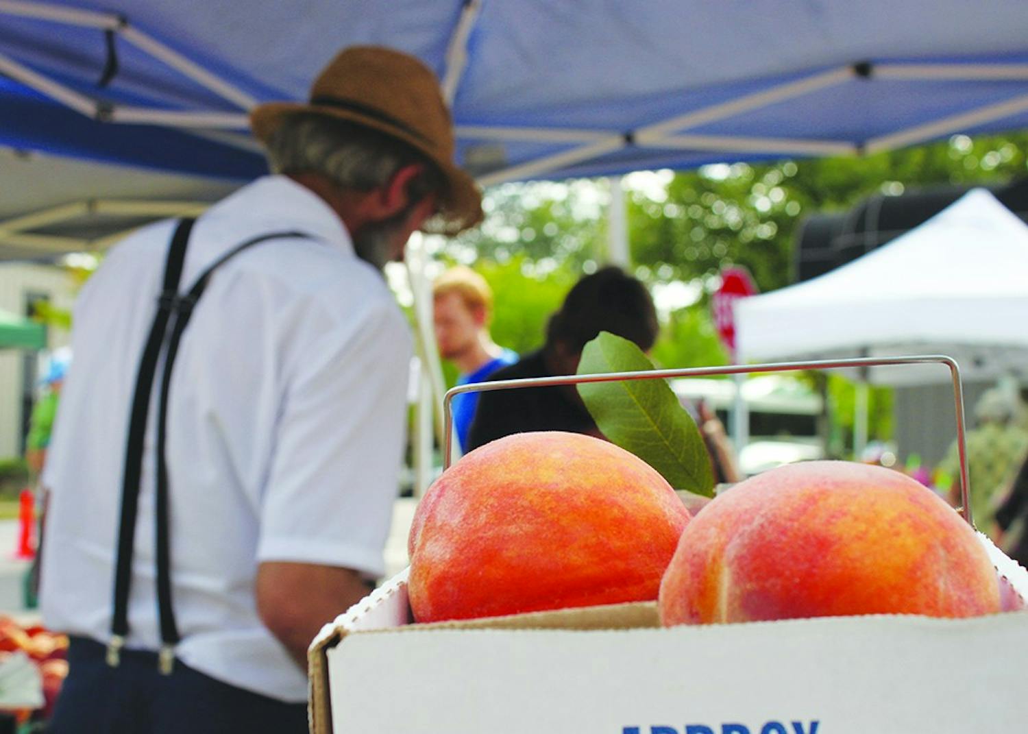 Daniel Graber sells fruit at the Bloomington Farmers' Market in 2013 in front of a box of peaches, his main crop. The city's director of economic and sustainability development discussed the city's solar energy initiative at Saturday's market.