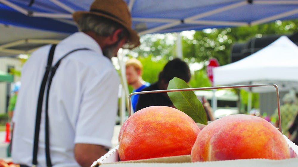 2013年，丹尼尔·格雷伯(Daniel Graber)在布卢明顿农贸市场(Bloomington Farmers’Market)卖水果，他站在一箱桃子前，桃子是他的主要作物。该市经济和可持续发展主任在周六的市场上讨论了该市的太阳能计划。