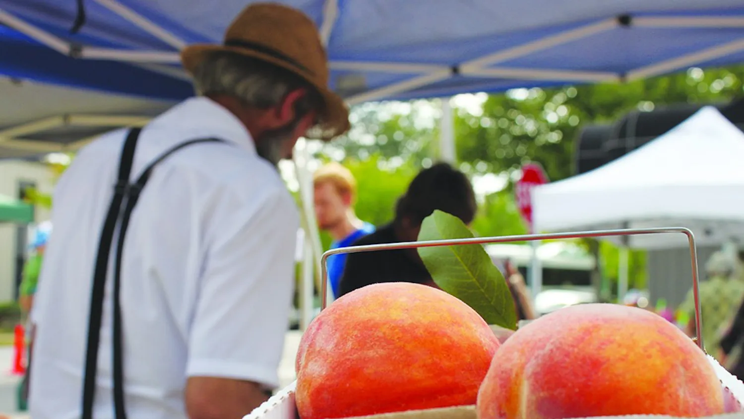 Daniel Graber sells fruit at the Bloomington Farmers' Market in 2013 in front of a box of peaches, his main crop. The city's director of economic and sustainability development discussed the city's solar energy initiative at Saturday's market.