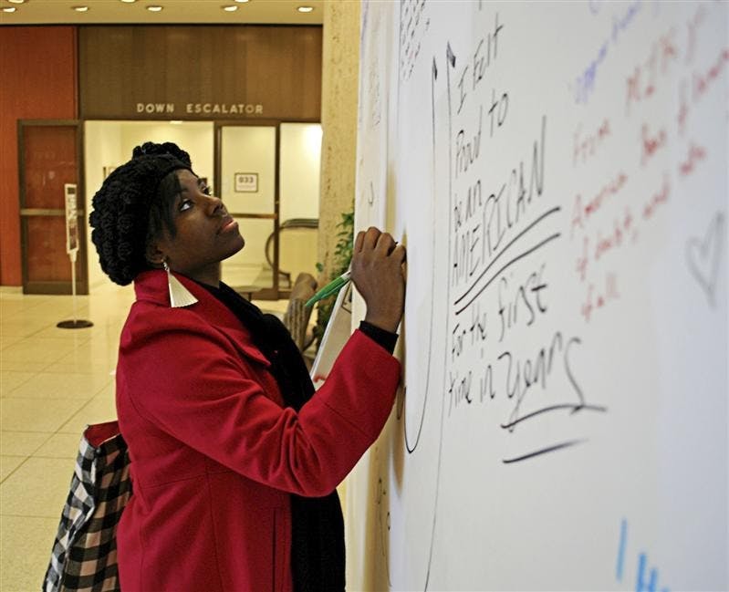 Senior Shyra Collins writes on the "Yes We Can" art project Tuesday afternoon in the main lobby of the Herman B. Wells library.