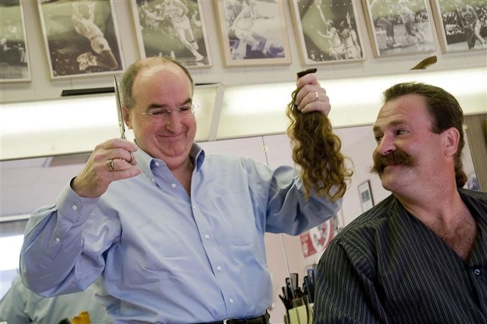 IU President Michael McRobbie, left, smiles after cutting the hair of his barber Frank Meadows Friday morning at Crosstown Barber Shop. Meadows, who grew his hair for more than 2 years, plans to donate his hair to Locks of Love.