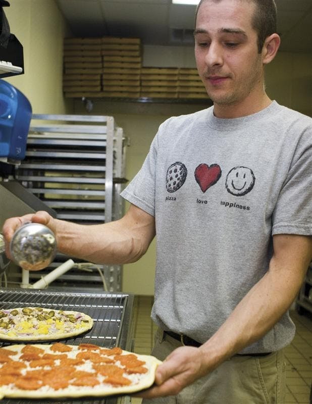 Pizza Express employee John Reidy puts the final touches on a pizza before putting it in the oven at the Pizza Express on East Tenth Street.  