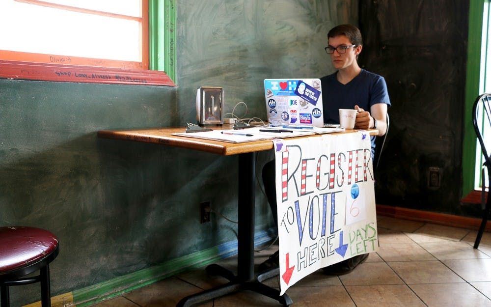 Kegan Ferguson, a senior in law and public policy, tends a voter registration booth Wednesday afternoon. Volunteers from IU Dems took shifts between 3 and 7 pm at Baked! of Bloomington on 3rd Street. 