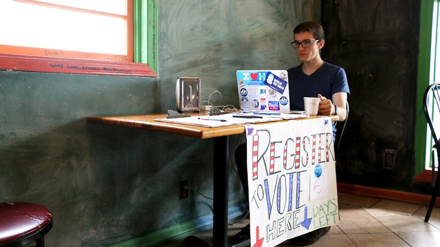 Kegan Ferguson, a senior in law and public policy, tends a voter registration booth Wednesday afternoon. Volunteers from IU Dems took shifts between 3 and 7 pm at Baked! of Bloomington on 3rd Street.
