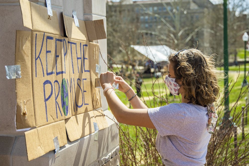 <p>Then-freshman Annetta Itnyre, a member of Students for a New Green World, tapes a sign to a pillar outside Dunn Meadow on March 24. The sign reads &quot;Keep The Promise.&quot; </p>