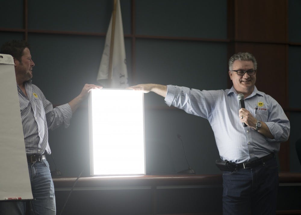 Rex Barnes and Jeff Goldsberry from Let It Shine Lighting hold up a hi-bay LED light, commonly used in gyms and factories, at the Sustainable Profits forum Monday. Let It Shine Lighting and other local small business owners presented ways for business owners to save money by going green.&nbsp;