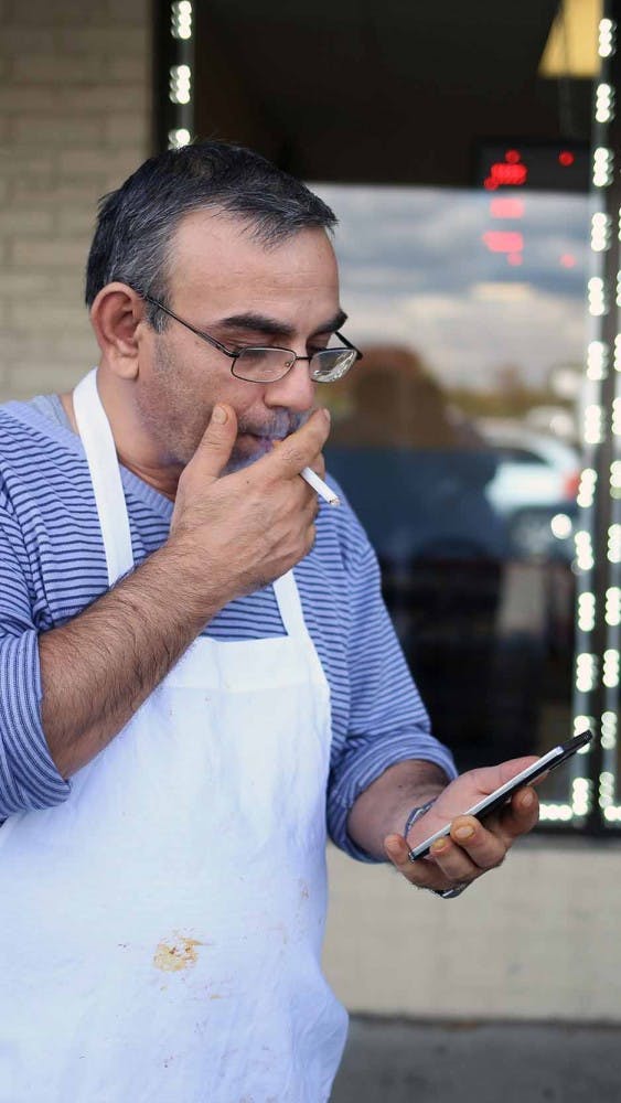 Marwan smokes a cigarette after his shift on Oct. 17 outside the restaurant he works at. He's checking his phone - one of the few ways he has of staying in touch with the news from back home. 