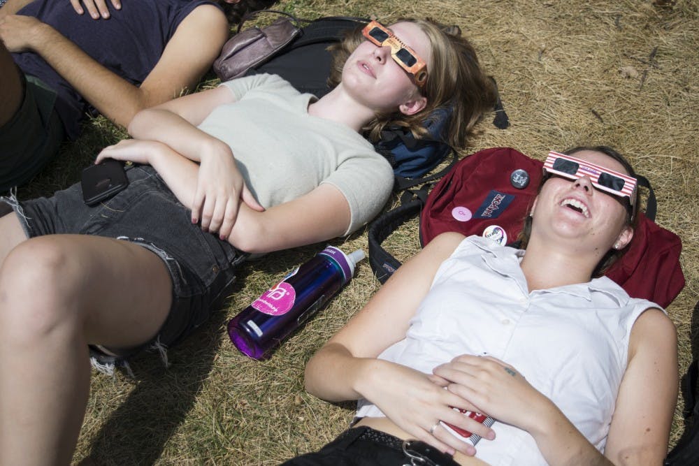 Students wearing eclipse sun glasses laying in the grass while watching the eclipse.