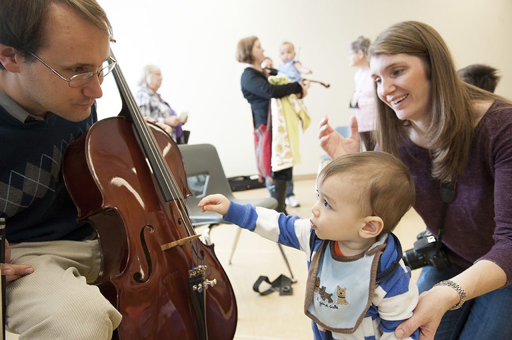 Joellan Chang watches on as her son, Sam, tries to pluck the strings of a cello at Wonderlab's "Meet the Instruments" event Saturday.