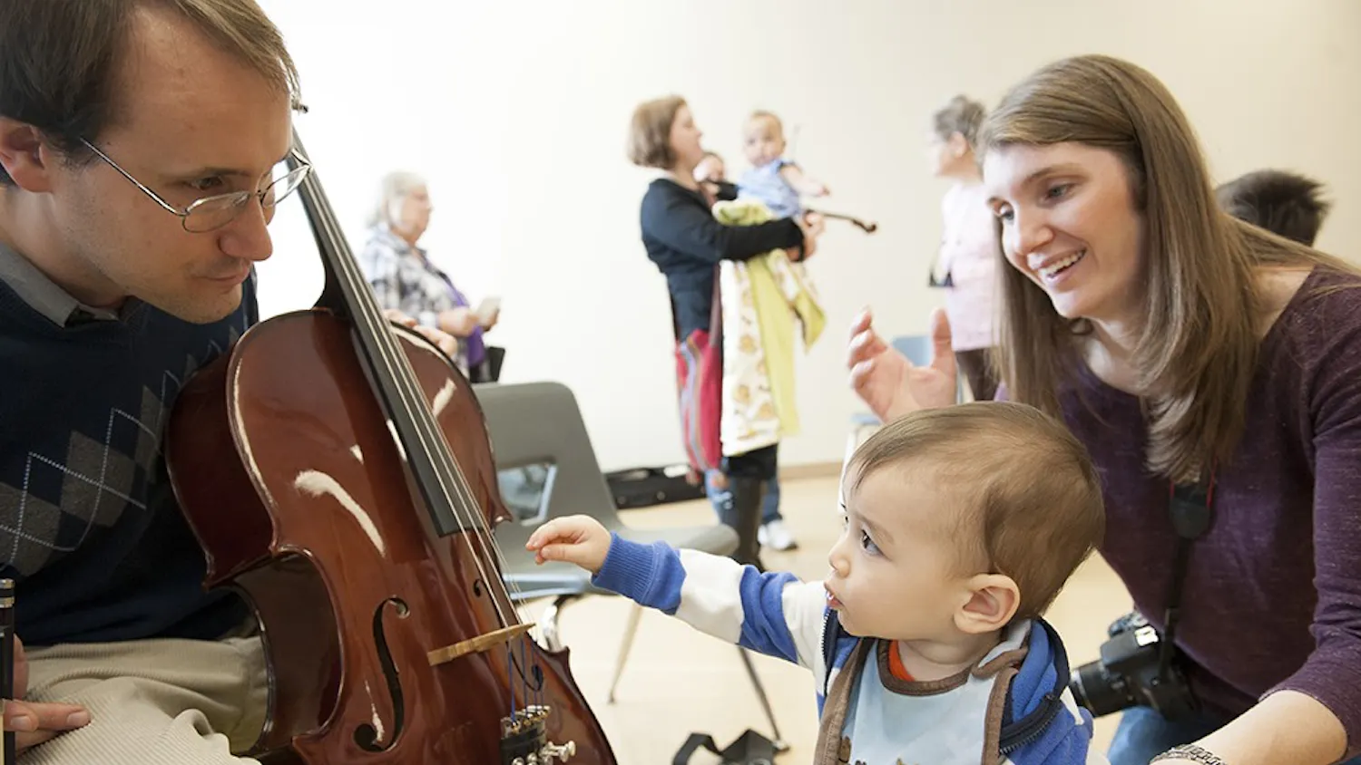Joellan Chang watches on as her son, Sam, tries to pluck the strings of a cello at Wonderlab's "Meet the Instruments" event Saturday.