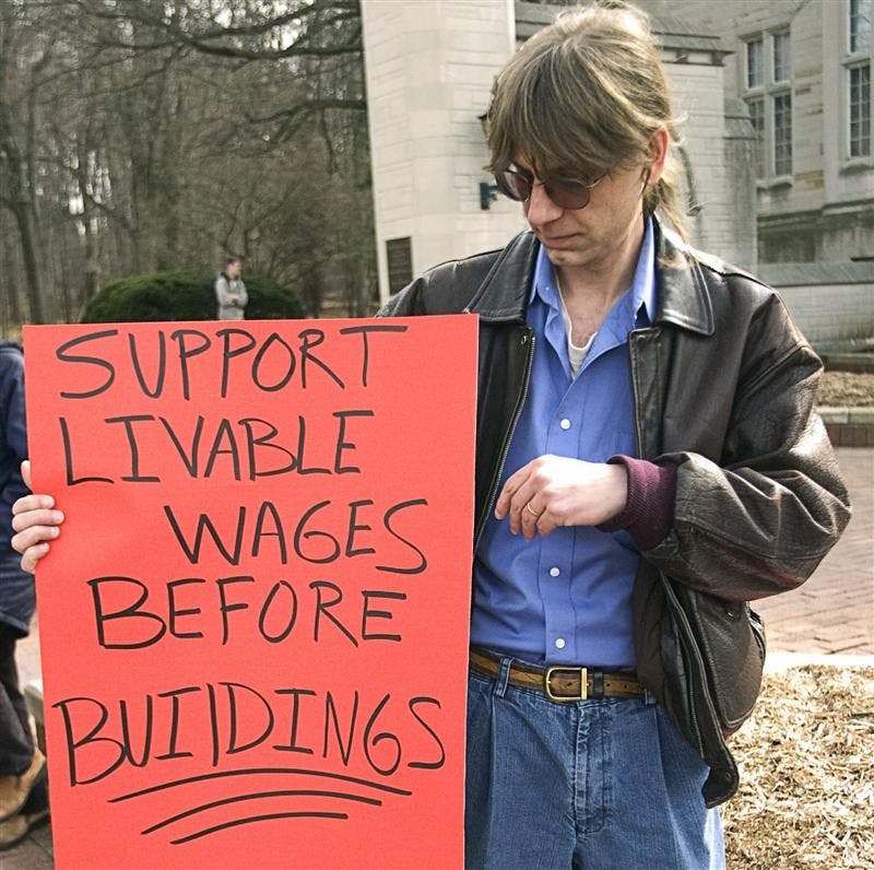 Peter Kaczmarczyk holds a sign Friday afternoon at the Sample Gates. Protesters gathered to speak out about the wages of IU and decisions to spend money on buildings.