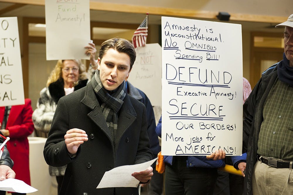 Sophomore Andrew Ireland reads a message protesting against the executive order on immigration passed by President Obama on Wednesday. The rally held in front of Todd Young's Bloomington office was organized by the Bloomington Grassroots Conservatives.