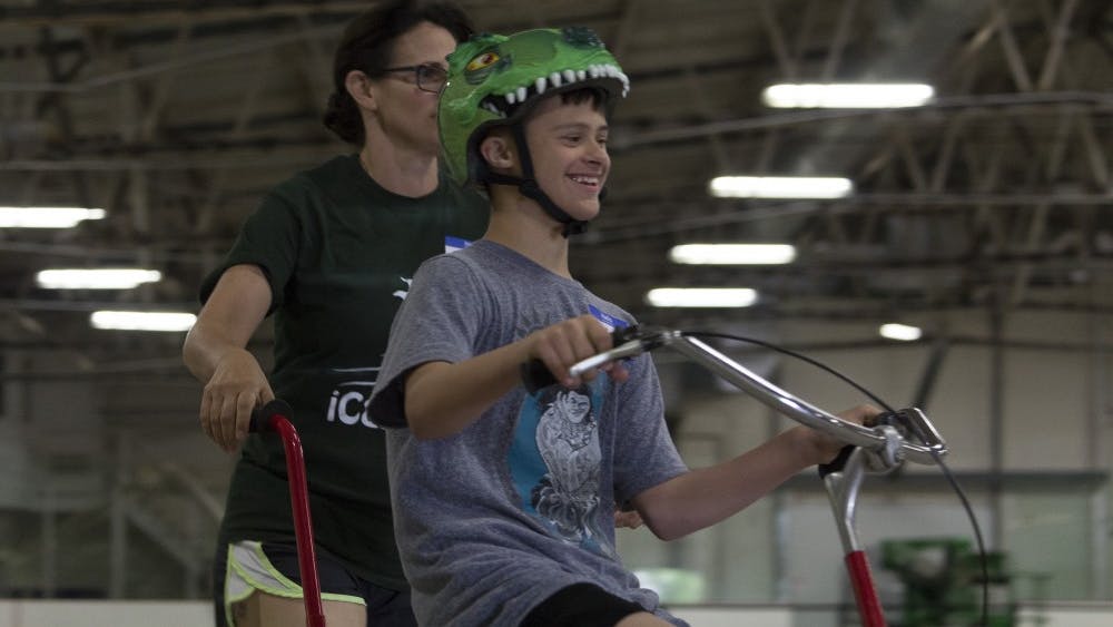 Jake Halvorson (right) rides alongside his mother, Lisa Halvorson (left), at the iCan Bike Camp on Thursday, May 17, in the Frank Southern Ice Arena. The camp teaches confidence and bike riding to people with disabilities.&nbsp;