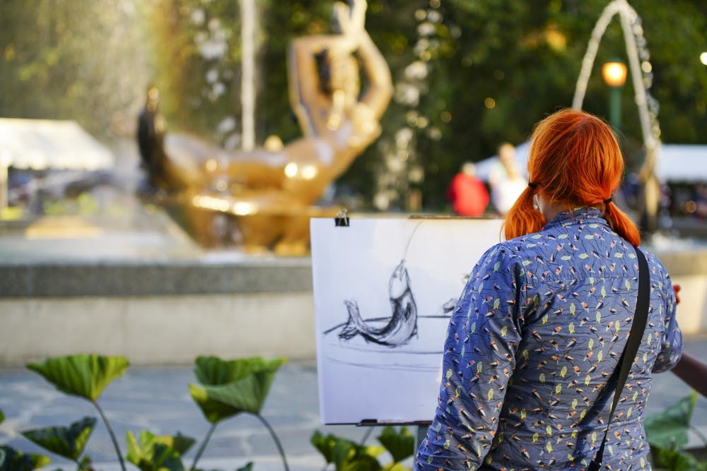 <p>WFIU employee Kayte Young composes her sketch of Showalter Fountain as the sun sets during the First Thursdays event Thursday evening in the Fine Arts Plaza. The monthly festival aims to bring the community together with live music, food and the arts.</p>