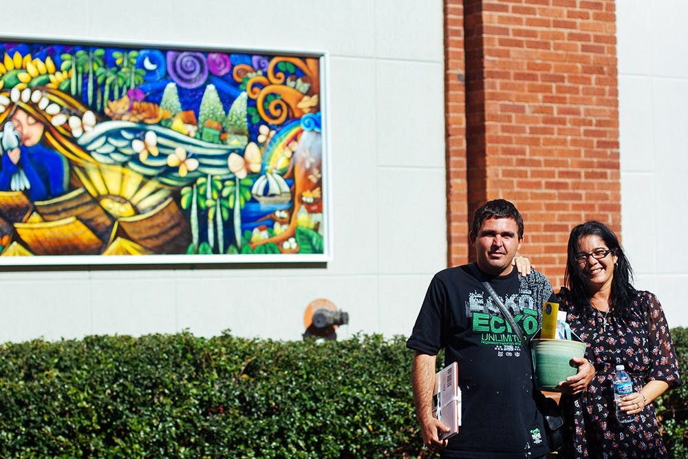 Cuban artists Madelin Perez Noa (and Leo Freire Leiva pose with Noa's mural "Si Hiciera Falta". The mural was permanently installed at the Bloomington Convention Center to recognize the importance of Bloomington's relationship with Santa Clara, Cuba, as well as strengthen the community's promotion of the arts.