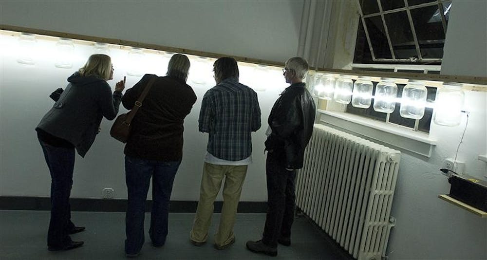 Visitors look at a pickle jar art lighting installment by Chicago professional artist Jason Kravarty during the display's opening Friday evening in the McCalla School at 10th Street and Indiana Avenue. The lighting, which is run on a 15,000 high volt low amp power box, will stay on display for two weeks.