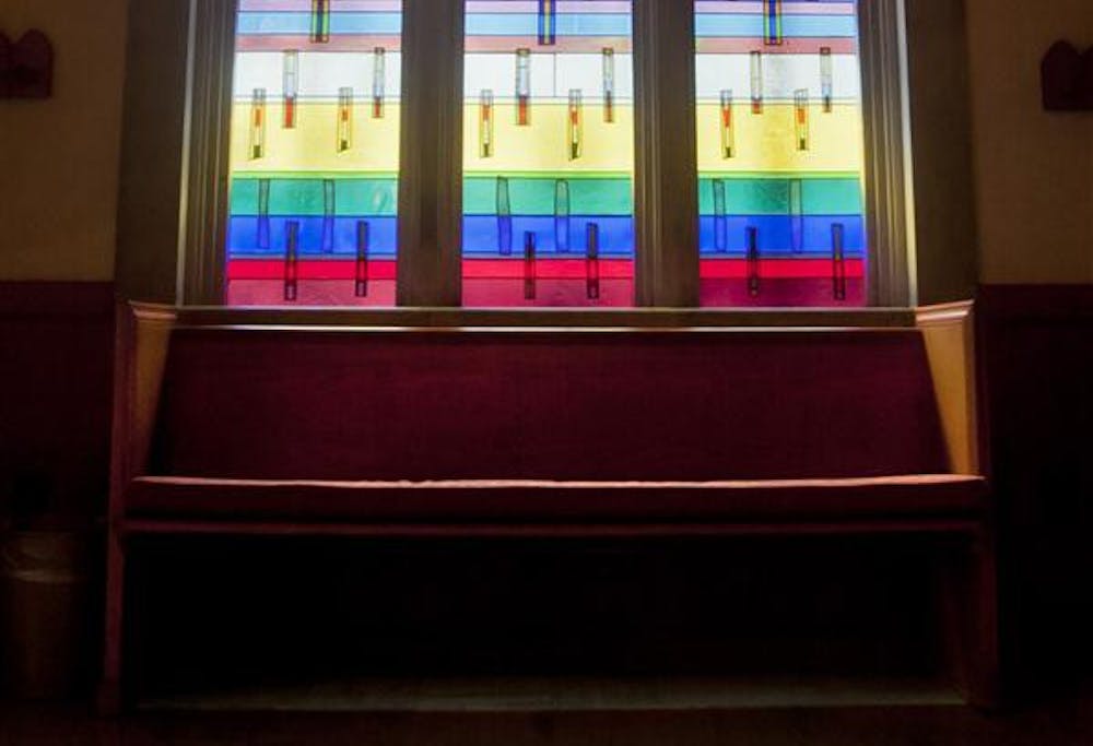 <p>The sun shines through stained glass behind a pew. </p>