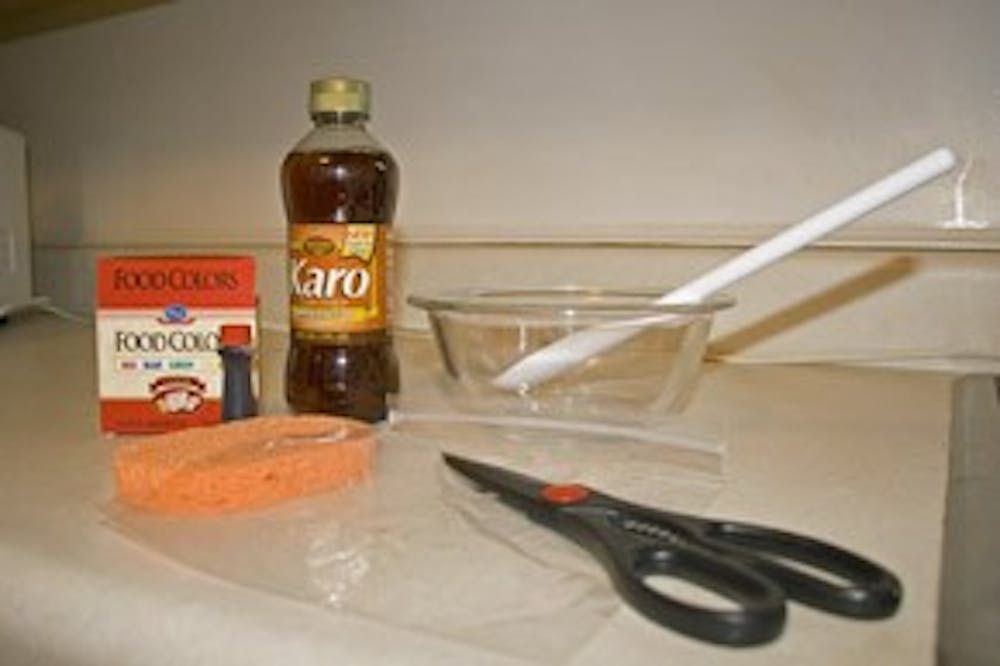 To get started, grab some dark-colored corn syrup (we chose Karo brand with brown sugar) and a whole box of red food coloring. Get your utensils: bowl, spoon, sponge, baggie, scissors.