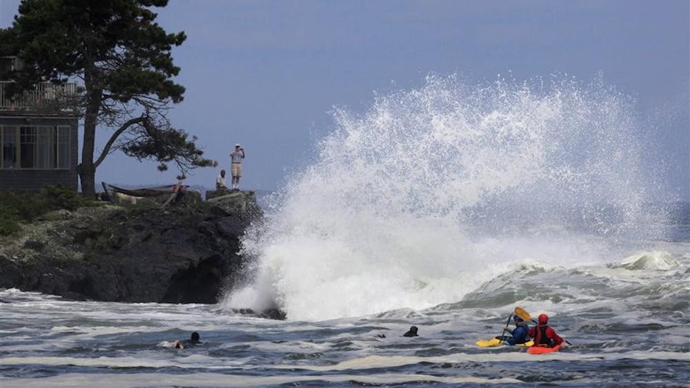 A man photographs heavy surf generated by Hurricane Bill while kayakers and surfers wait for a wave to ride Sunday in Cape Elizabeth, Maine. Officials say a large wave in Maine's Acadia National Park swept five people into the sea and three are still missing.