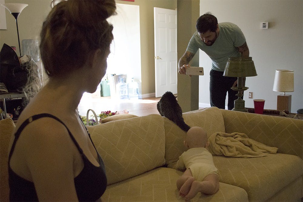 Mike Bridavsky takes video of Lil BUB jumping from the couch as his wife, Stacy, and baby, Rosco, look on. Due to her multiple disabilities, BUB does not often have the ability to do many things on her own and is largely dependent on Mike.