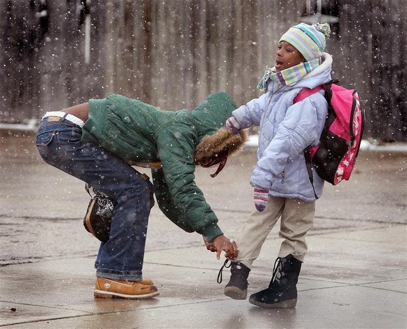 As the snow falls, Princess Witt, 23, of South Bend, Ind., ties the boot laces of her daughter, Alyssa Emerson, 5, after meeting her after school Monday at the bus stop in South Bend, Ind.