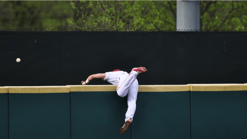 Alex Krupa falls over the left field wall chasing a Minnesota home run in the first inning Friday night. The Hoosiers lost 11-0 on Friday and rebounded with a 13-12 win Saturday.