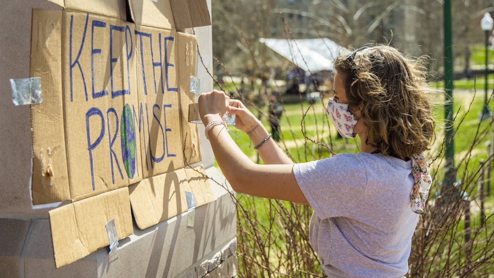 Then-freshman Annetta Itnyre, member of Students for a New Green World, tapes a sign to a pillar outside Dunn Meadow on March 24, 2021. Climate groups such as Students for a New Green World and Sunrise Bloomington plan to organize protests this semester to pressure IU to divest from fossil fuels and create a formal climate action plan.