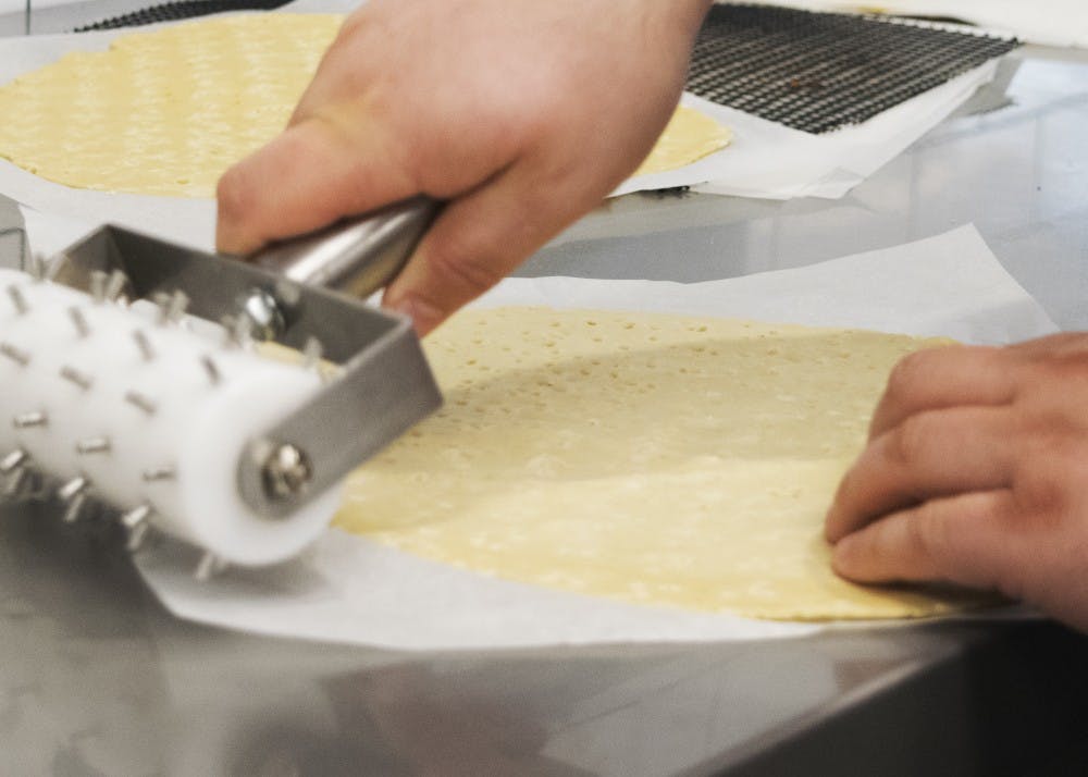 Elpers uses a docker to perforate the pizza dough. Doing so creates tiny dimples in the pizza that ensure the pizza bakes evenly and that bubbles don't develop in the dough while baking.