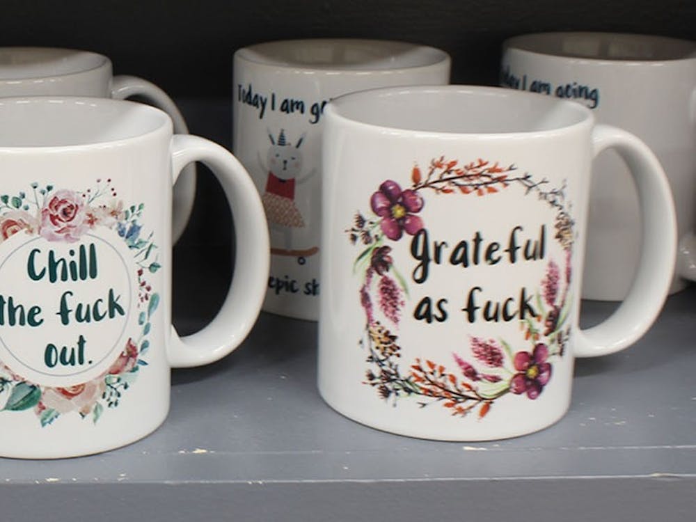 An assortment of  not-safe-for-work, mugs fill a single shelf. The artist, Chicaloo Kate, said on her website  the main goal of her products is to make people laugh, think or both.