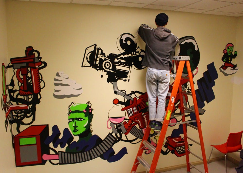 Mat Whiteley, a masters student in his third year, works on a mural in the stairwell of Franklin Hall. Whiteley spent months working on his artwork, then printed it on giant stickers to put on the wall.&nbsp;
