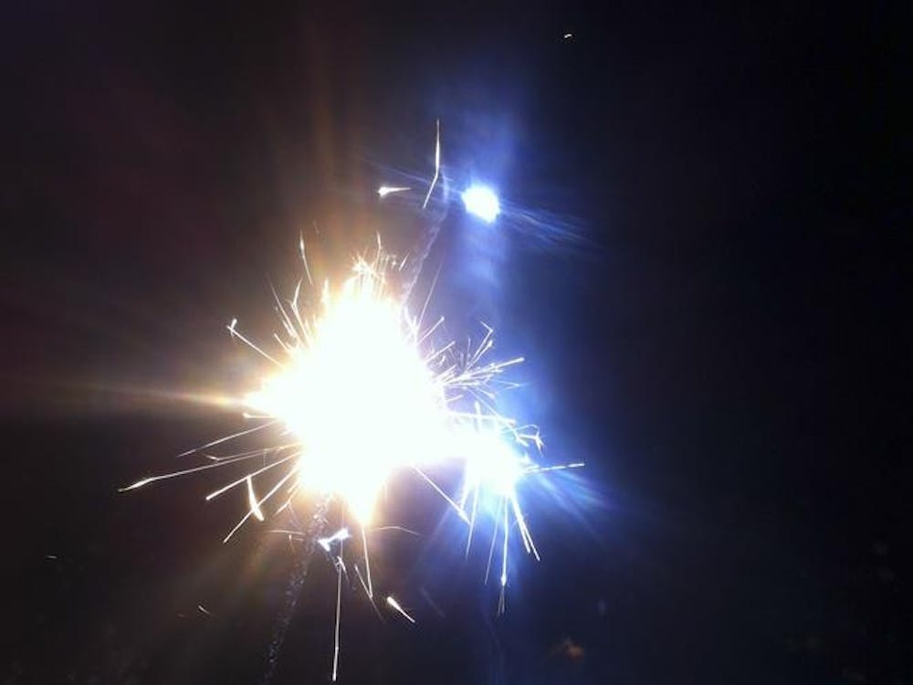 I hold a sparkler at arm's lengh while our neighbors set off firecrakers in the background.