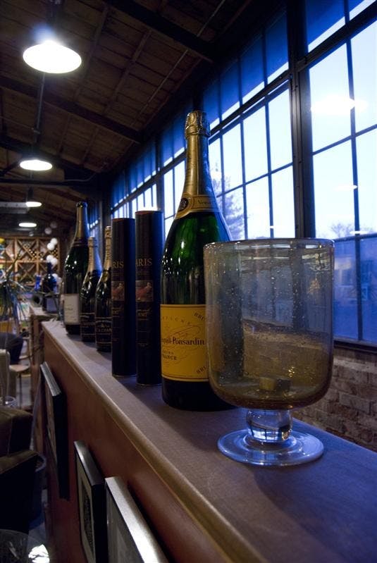 Wine bottles and glasses stand on a coppertop counter at Tutto Bène located at Third and Rogers streets. Starting Tuesday, the popular restaurant will provide food and wine specials as part of Customer Appreciation Week before it closes Saturday.