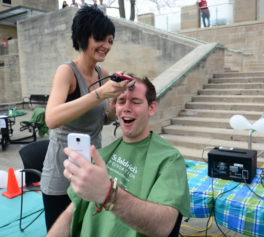 George Sprague, resident manager of Forest Residence Center, takes a video of himself getting shaved by Jackie Aynes, volunteer barber of the event, on Sunday afternoon at IU Teter Beach. “It’s really refreshing,” Sprague said after he shaved his head. 
