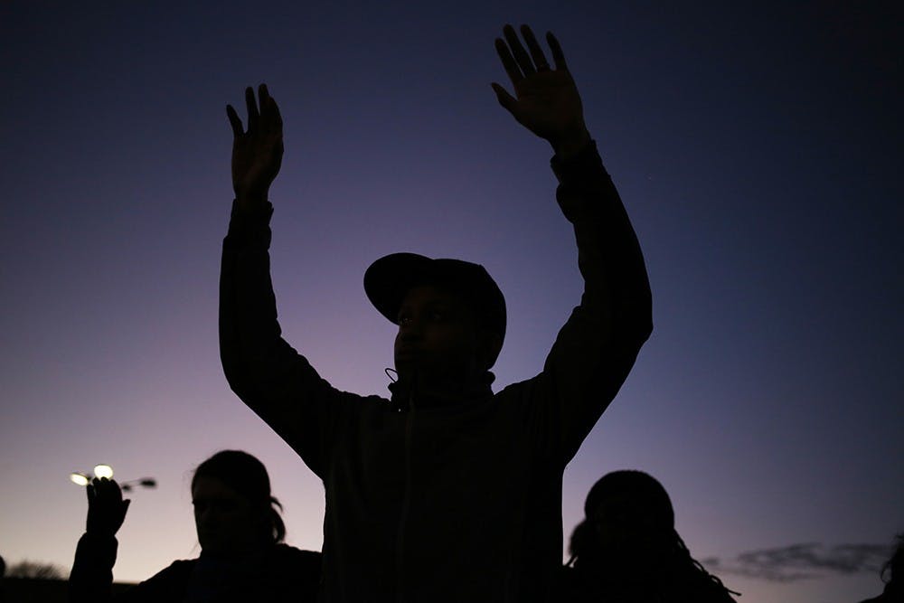 A protester raises his hands in the "Hands up, don't shoot" gesture during a four and a half-minute moment of silence in remembrance of Michael Brown, whose body reportedly lay in the street for over four hours after his death, on College Mall Road on Monday evening. 