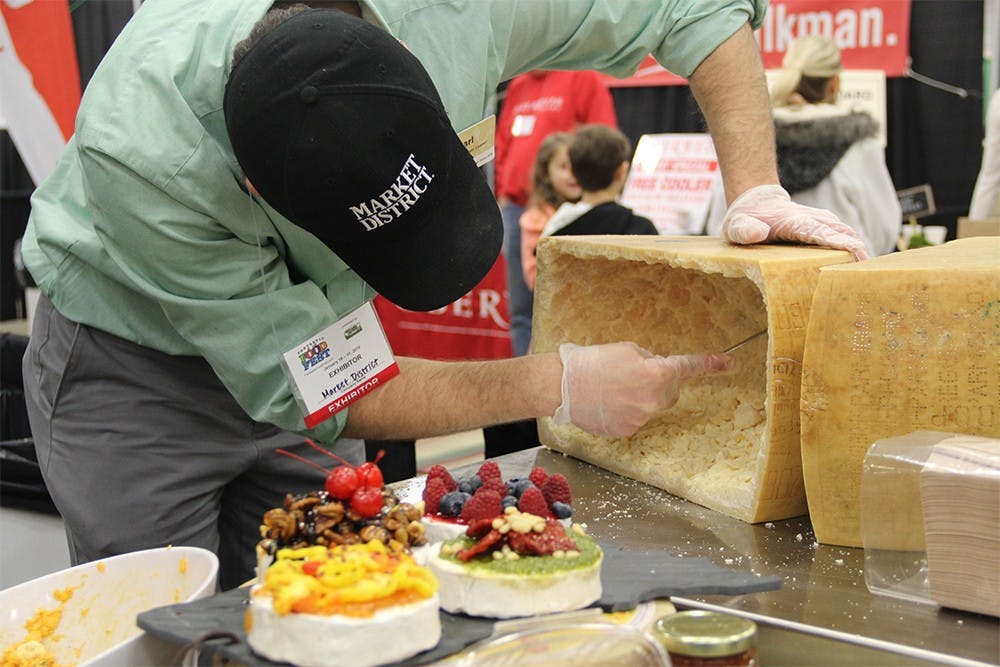 An Indiana Grown employee scrapes cheese out of a wheel for attendees of the Indianapolis Fantastic Food Fest Saturday. The vendors said they had distributed about 80 pounds of cheese over the weekend. 