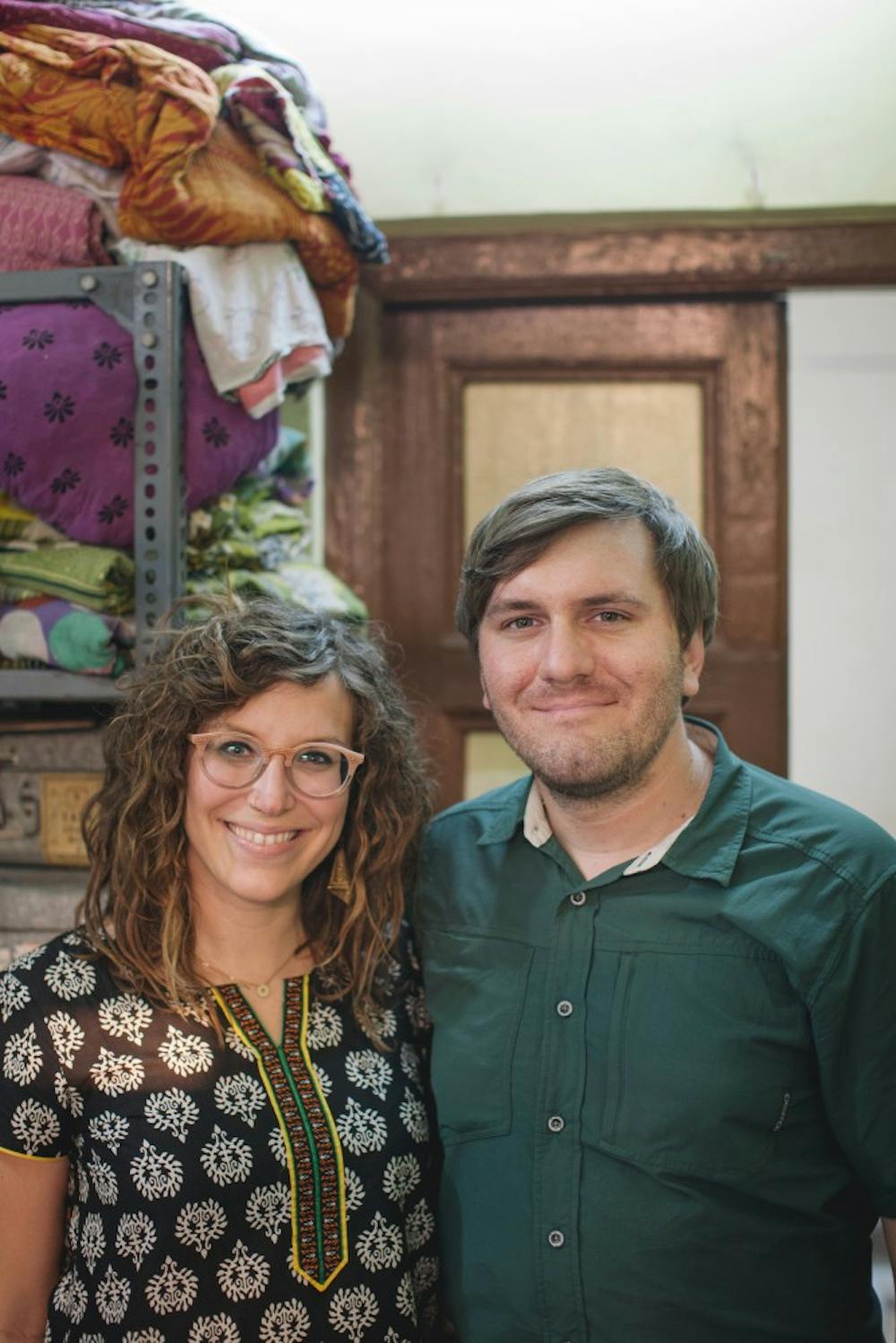 Photographers Frank and Sarah Schweikhardt stand in front of blankets made by women from Sari Bari, an organization that helps women in India leave the sex trafficking by training them as artisans. The photos documenting their time at Sari Bari will be displayed in downtown Bloomington at Gather until Jan. 31.