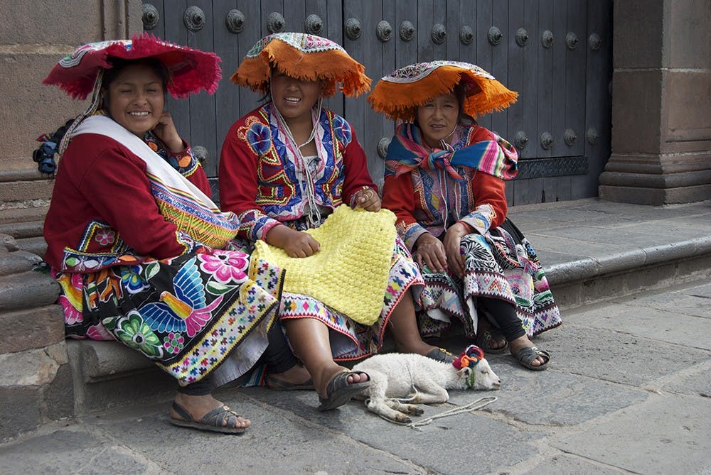 Women in traditional clothes sit on one of the streets of Cuzco with a lamb, allowing passing visitors to pet it and hold it for a couple soles, the Peruvian currency.