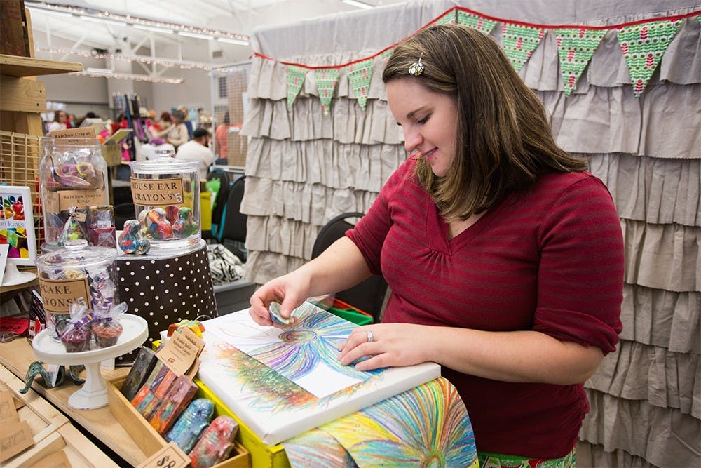 Artist Nicole Lewis draws rainbow flowers with her handmade rainbow crayon at the Bloomington Handmade Market on Nov. 8, 2014. "Art 2 the Extreme" features recycled, rainbow crayon creations in over 175 shapes and sizes. Teacher by day and artist by night, Nicole creates fun and unique gifts for all ages and interests. From crayon rings to giant, crayon robots, there is something for everyone to enjoy in their stocking this holiday." ( Bloomington Handmade Market Guide Book, 47)