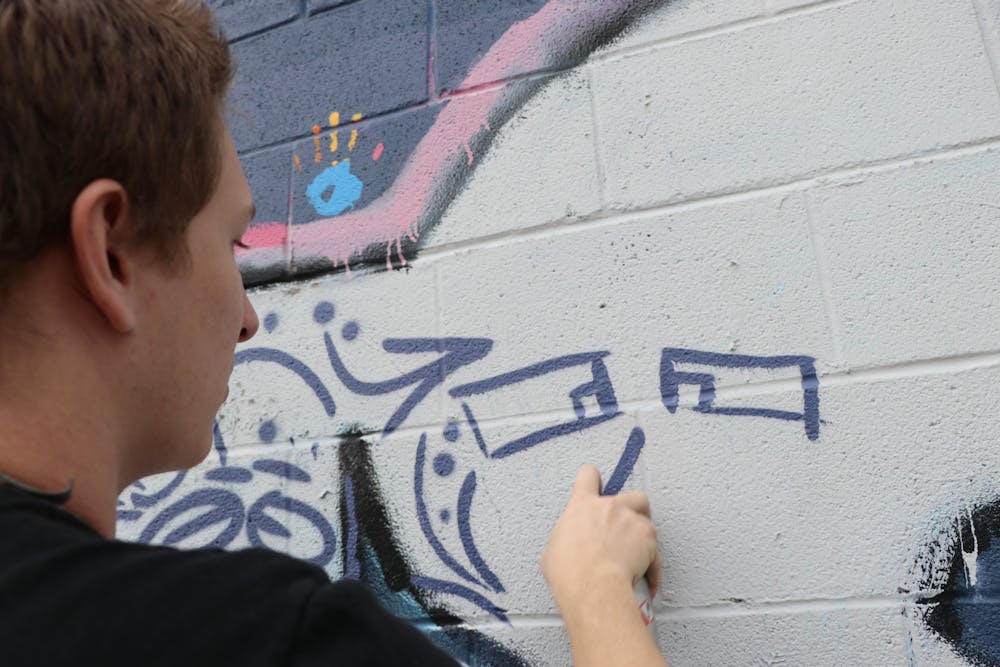 Then-IU sophomore Trenton Musch works on a mural Nov. 20, 2020 outside of The Warehouse in Bloomington. The Bloomington Creative Glass Center will put on a paint-by-numbers mural community event Saturday.
