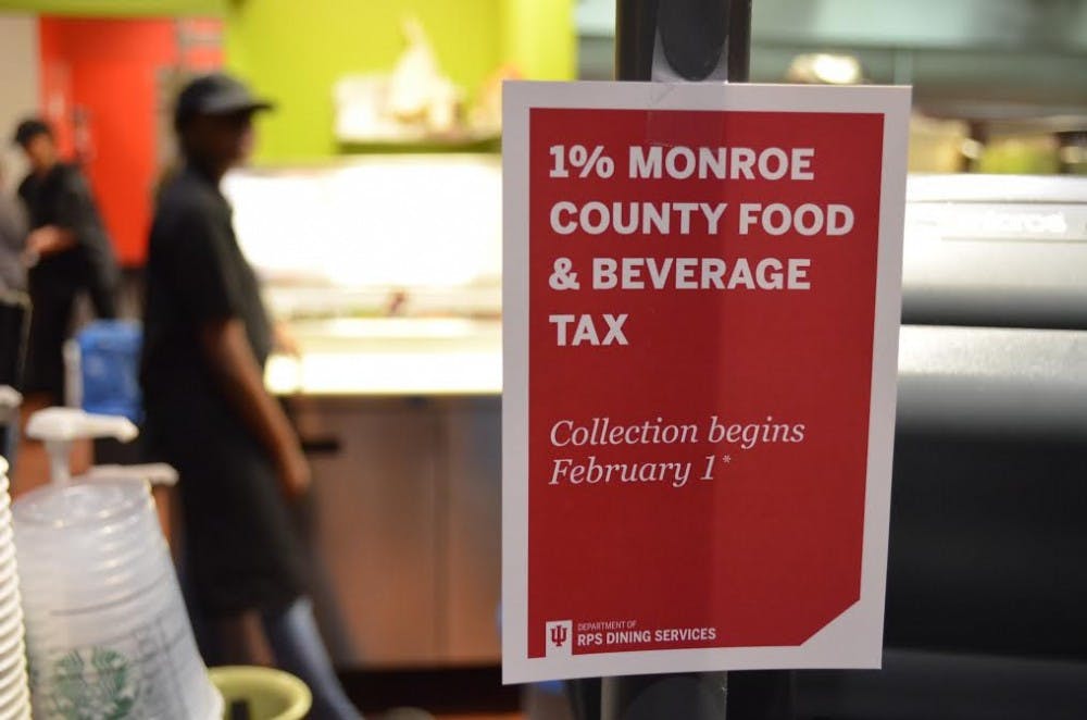 <p>A sign hangs on the cash register of The Round café in Forest Residence Center informs students of the new Monroe County food and beverage tax. The 1-percent tax will not apply to food courts or stores on the IU campus for current students.</p>