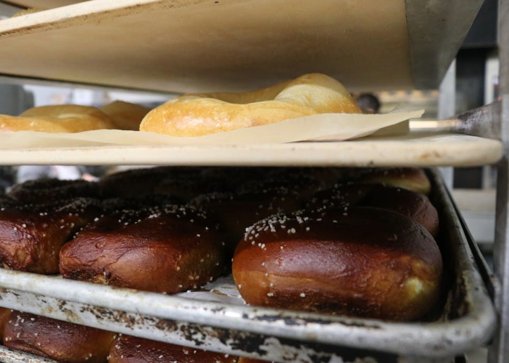 After being baked, the bagels are placed on racks or containers until they are picked up and delivered to one of four Bloomington Bagel Company locations. Pictured above are pretzel bagels and plain flagels, or flat bagels.