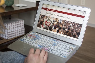 A student holds a computer displaying the Political and Civic Engagement website.